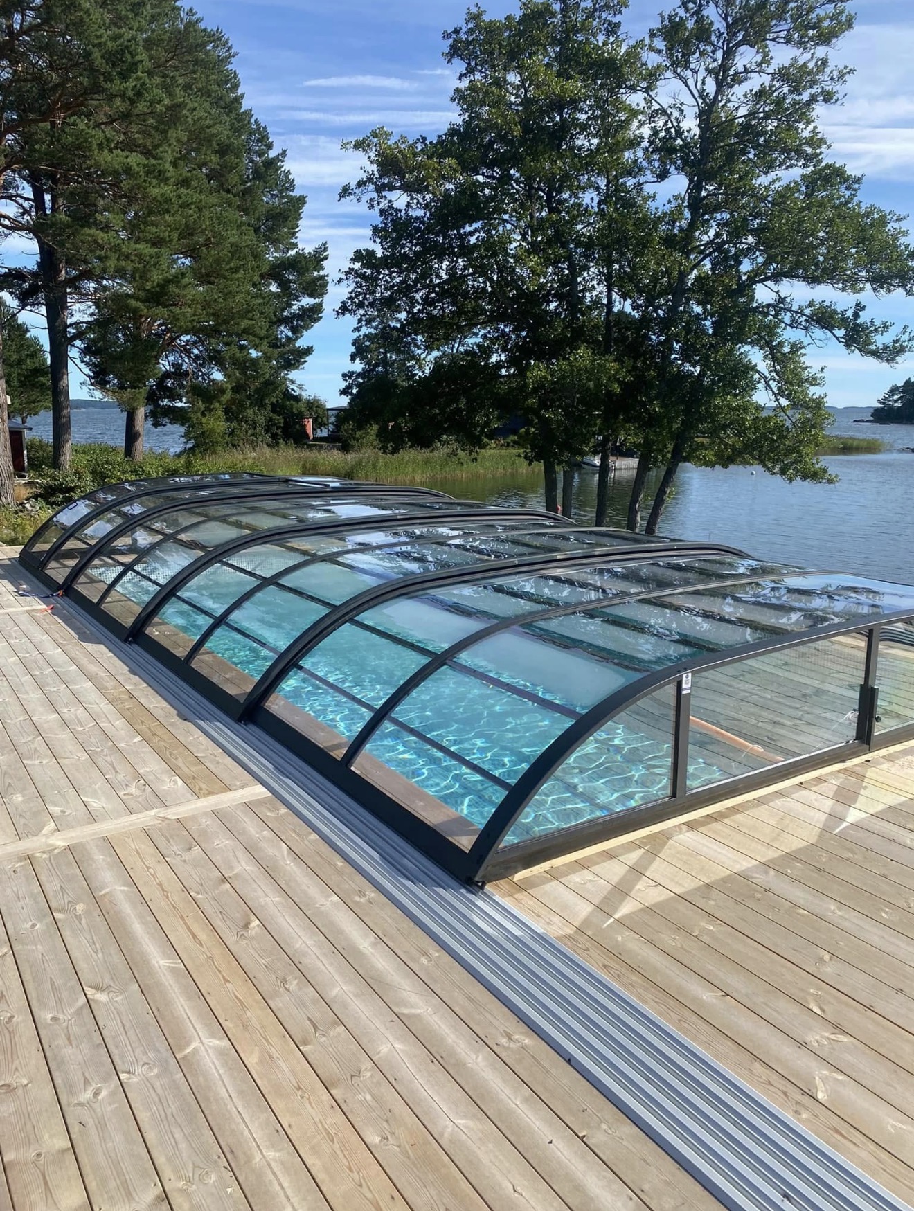 Pool med skjutbart pooltak och trädäck vid vattnet
